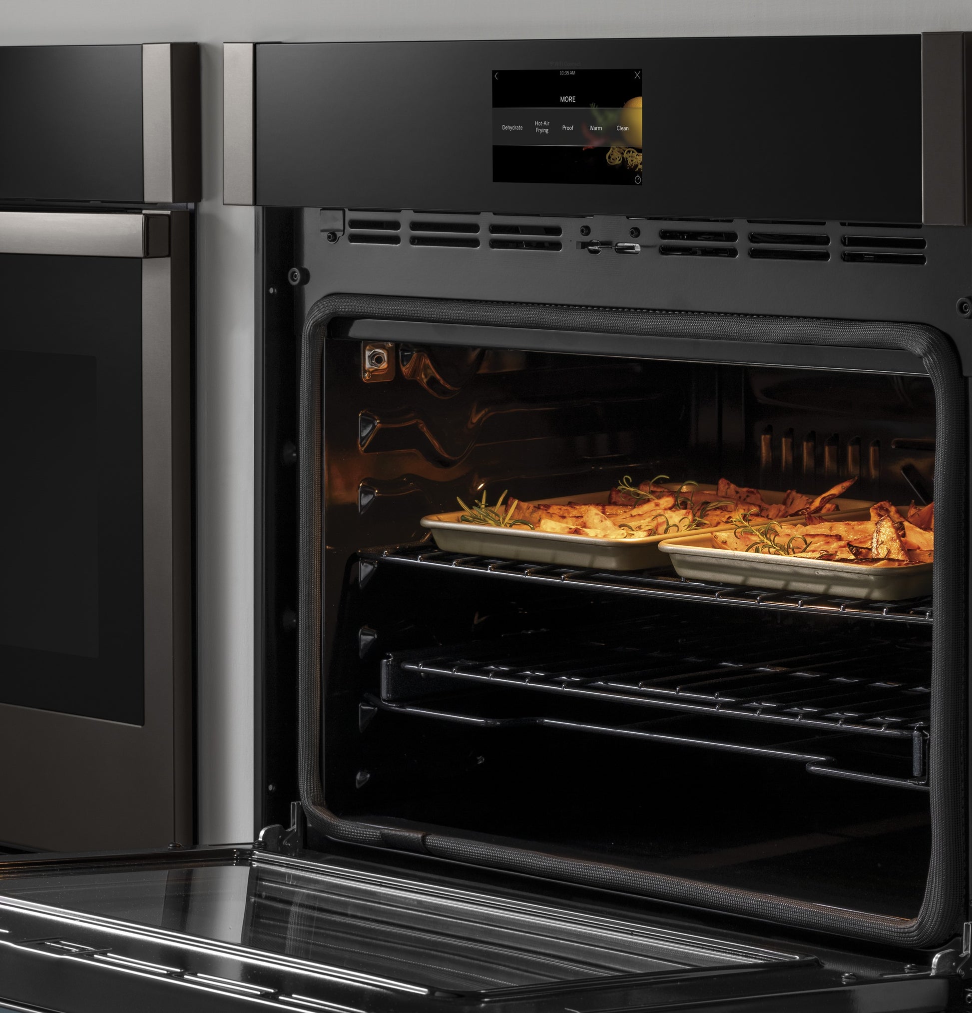 Open stainless steel built-in wall oven with trays of roasted food and digital control panel in kitchen appliances collection