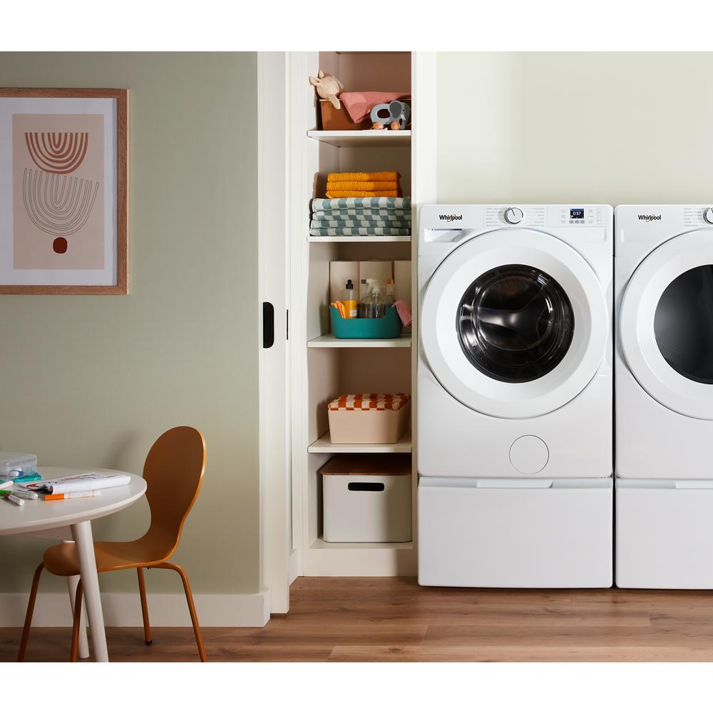 White front load washer with digital controls next to matching dryer in laundry room with shelving and chair