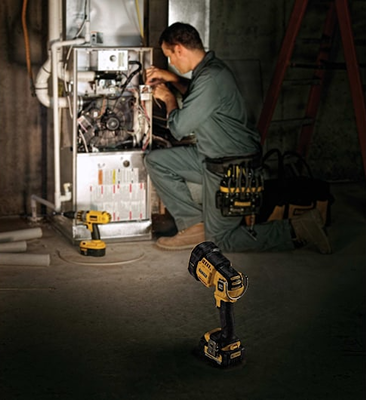 Cordless LED jobsite spotlight illuminating a technician repairing HVAC equipment in dim workspace