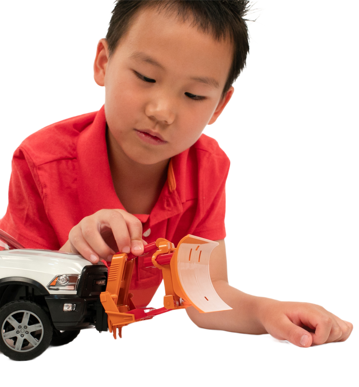 Child in red shirt attaching orange Bruder Toys plow blade to white toy truck for hands-on home improvement play