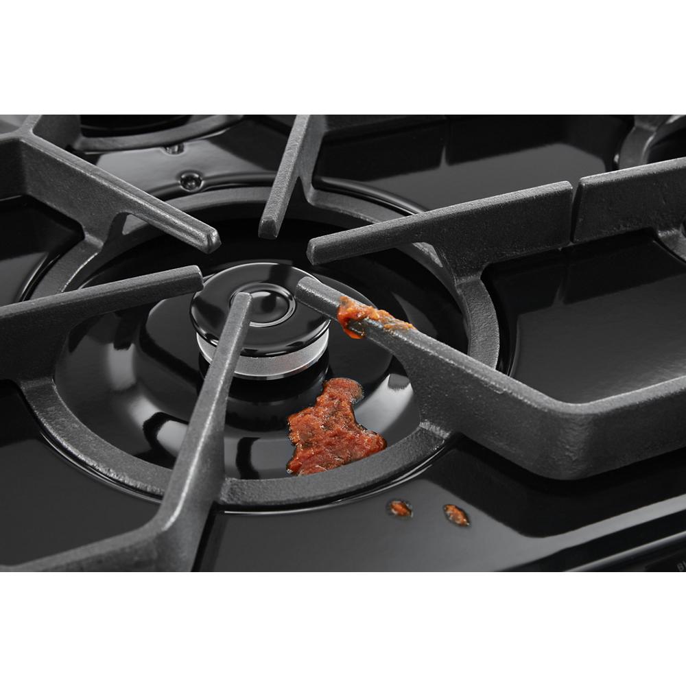 Close-up of a black gas range burner with sealed burners and visible food spill on the grates and surface