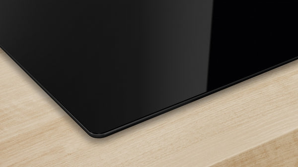 Black-glass electric cooktop with seamless design installed on light wood surface for kitchen improvement.