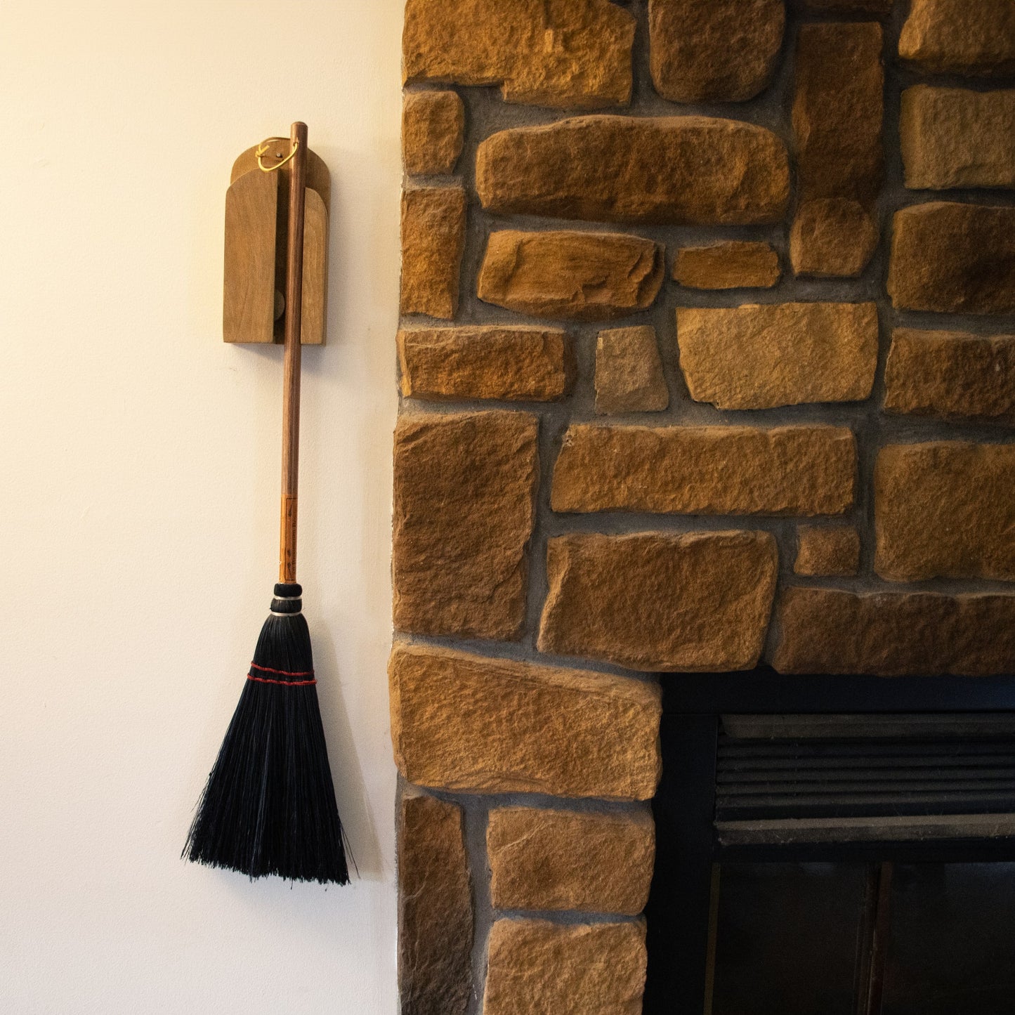Handcrafted wooden wall broom holder securing a broom beside a rustic stone fireplace in home improvement tools collection