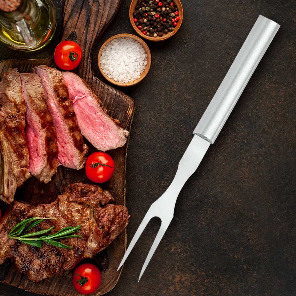 Two-pronged stainless steel carving fork with sleek handle beside sliced steak and cherry tomatoes in kitchen utensils collection