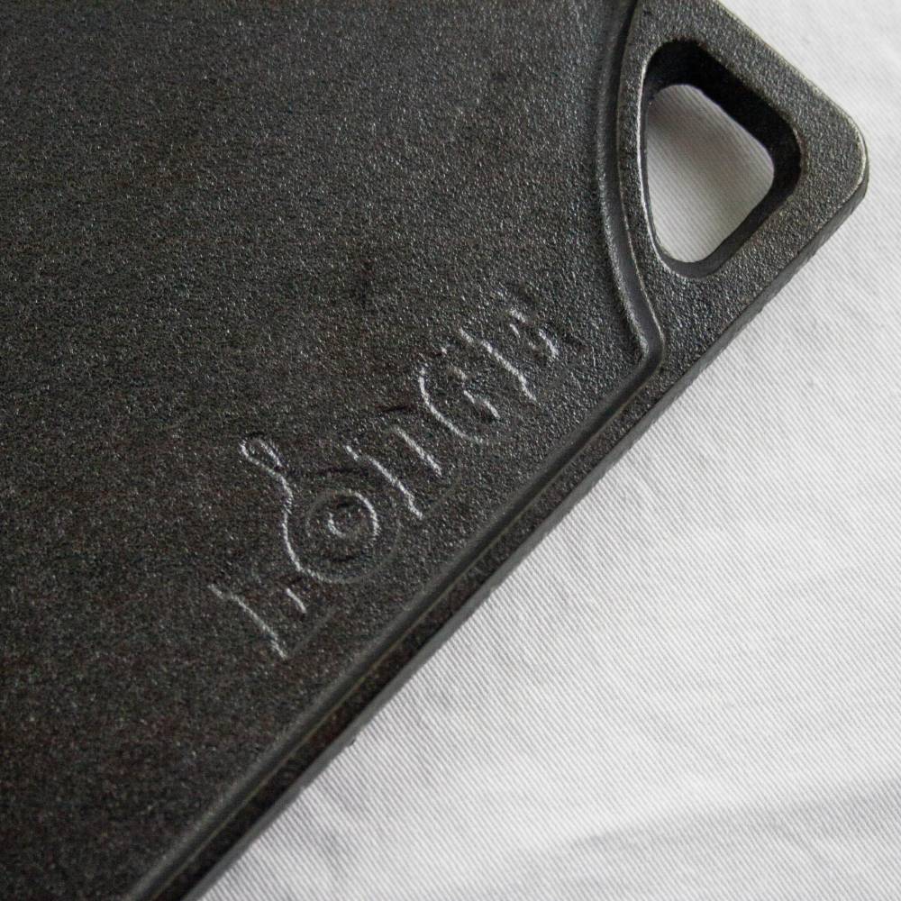 Close-up of corner handle and embossed logo on black cast iron griddle surface for home cooking and tools use