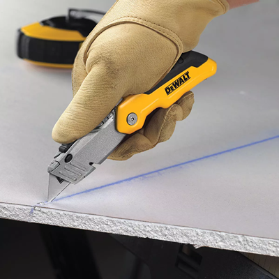 Hand gripping yellow and gray retractable folding utility knife cutting drywall panel in home improvement tools collection