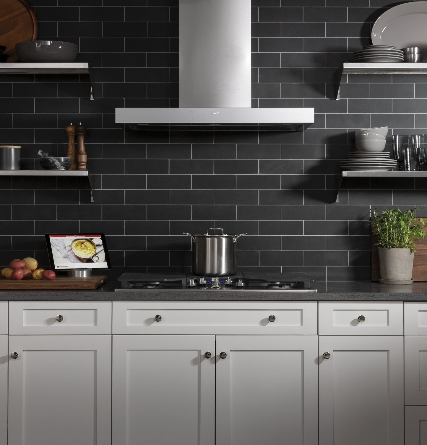 Modern kitchen with white cabinetry and dark subway tile backsplash featuring a sleek stainless steel wall mount hood
