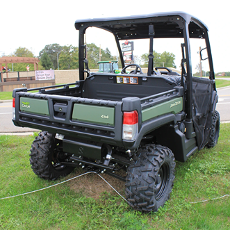 Green full-size utility vehicle with roof and rugged tires parked on grass near outdoor equipment display area