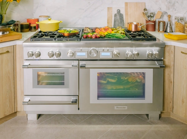 Stainless steel dual fuel range with double ovens, burners, and griddle in modern kitchen with wood cabinets
