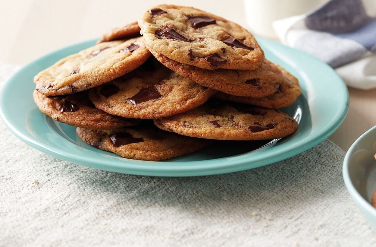 Freshly baked chocolate chip cookies stacked on a turquoise plate in a bright kitchen setting