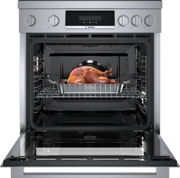 Open stainless steel freestanding induction range with ergonomic control knobs and a roast chicken inside the oven