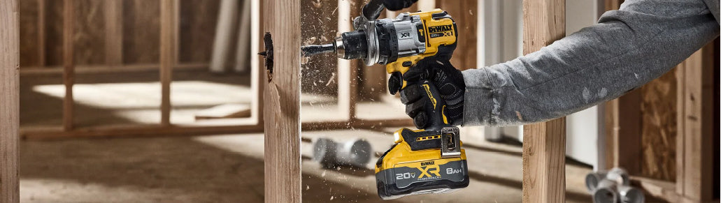 Close-up of a person using a yellow and black cordless drill to install wooden framing studs in a construction site with natural light.