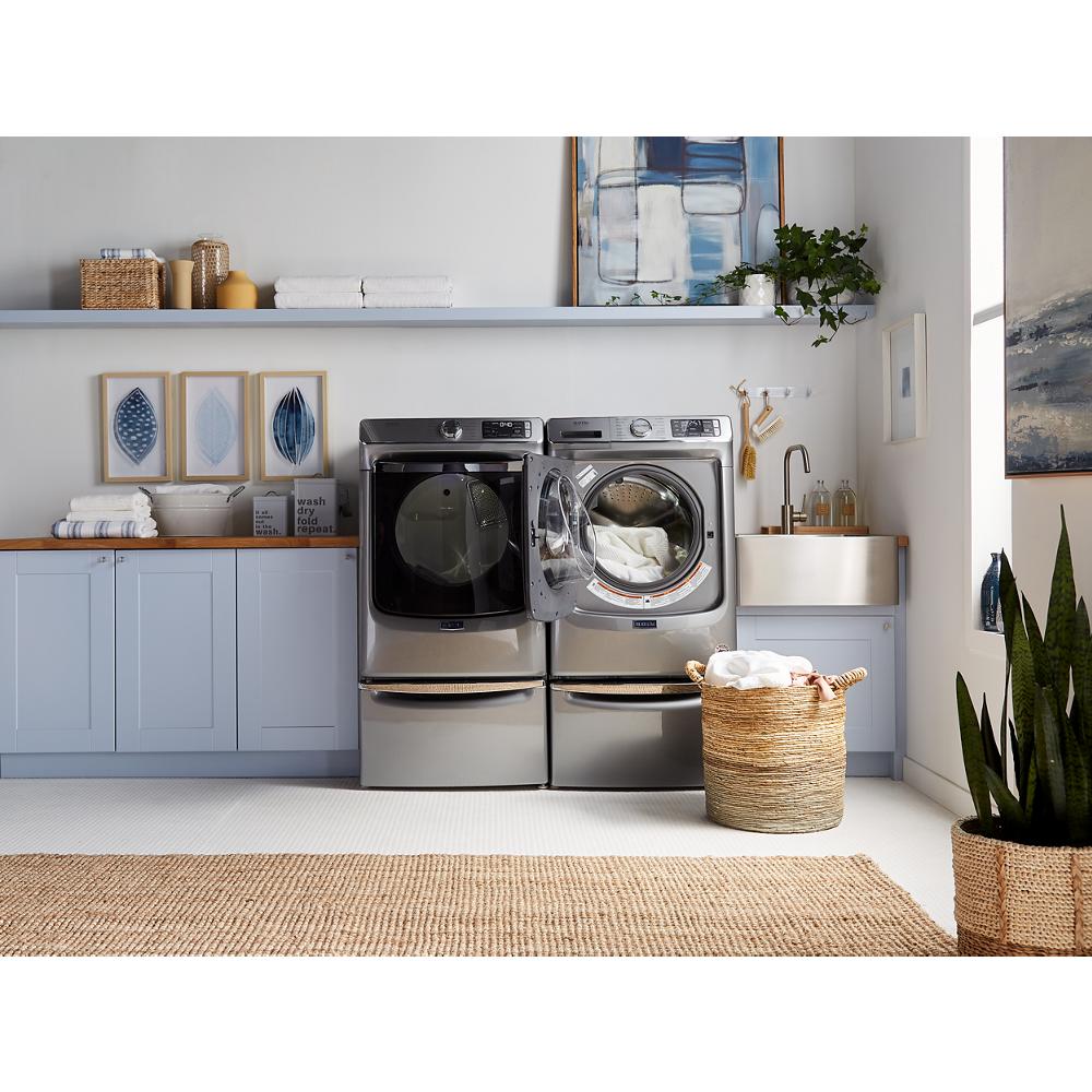Laundry room with stainless steel washer and dryer on pedestals, light blue cabinetry, and woven laundry baskets