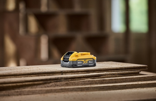 Compact yellow and gray 5Ah power tool battery resting on stacked wood boards in workshop setting