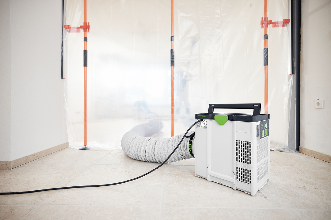 Compact air filtration unit connected to flexible hose inside room sealed for dust containment in home improvement setting