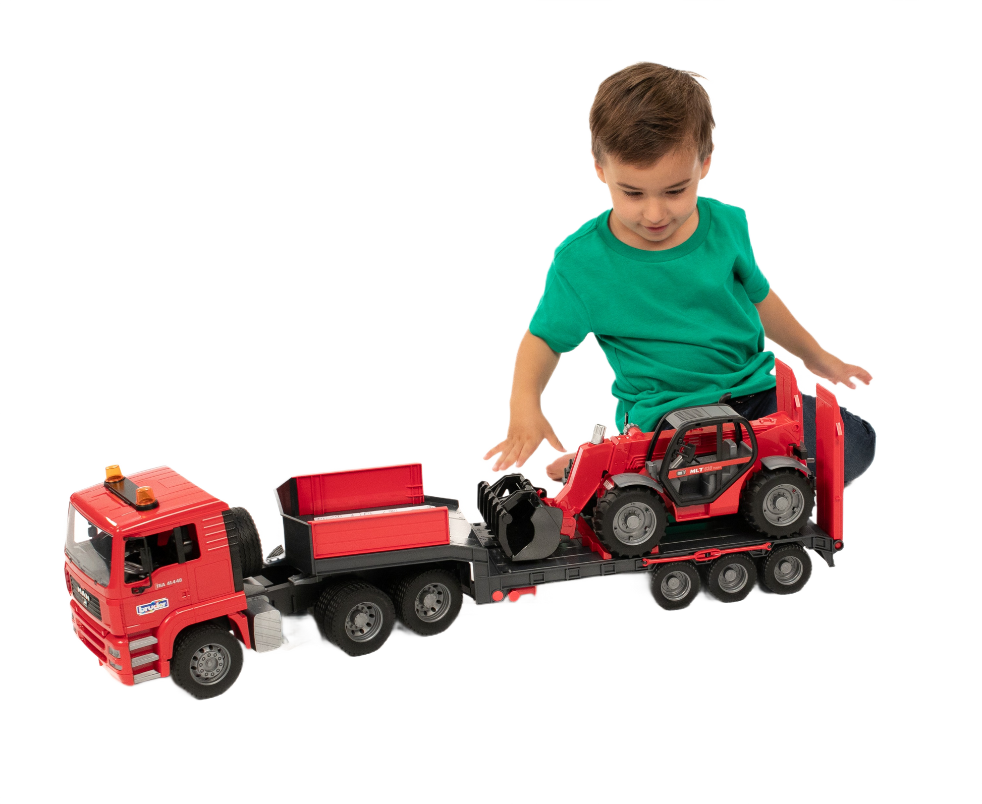 Child playing with red Bruder MAN TGA truck model carrying a compact red Manitou loader toy on flatbed trailer