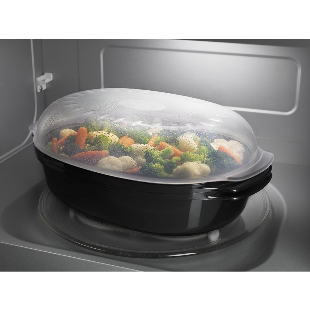 Black microwave steam cooking container with clear vented lid and mixed vegetables inside on glass tray