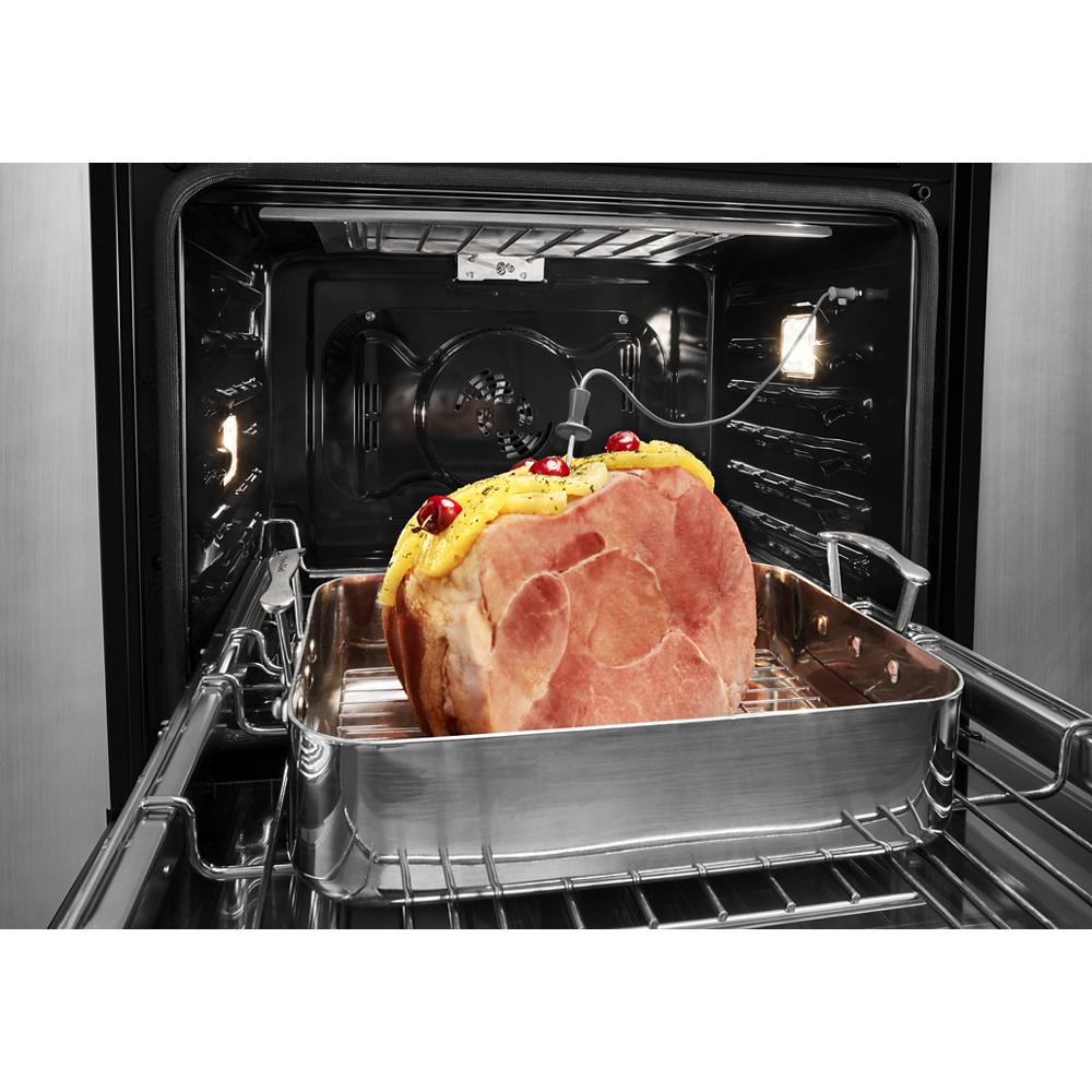 Inside view of stainless steel double wall oven cooking glazed ham on roasting pan with internal oven light on