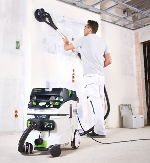 Person sanding drywall ceiling with Festool Planex sander and vacuum in unfinished construction space for home improvement