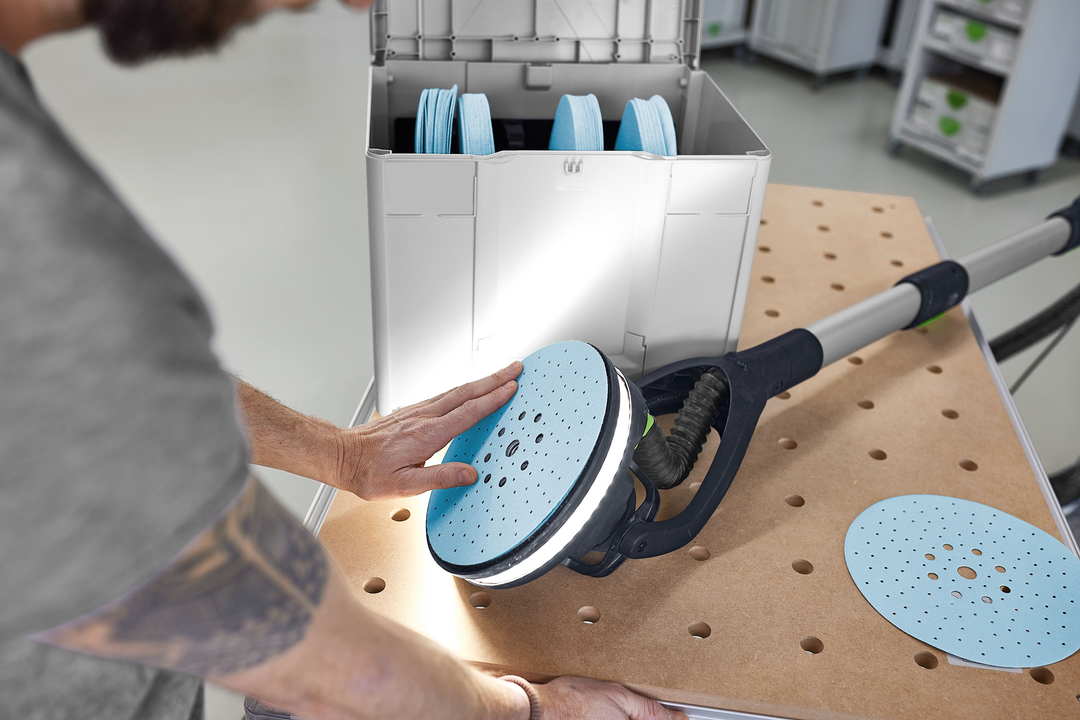 Person fitting blue abrasive disc onto long-reach sander near organized Festool Granat abrasives Systainer in workshop