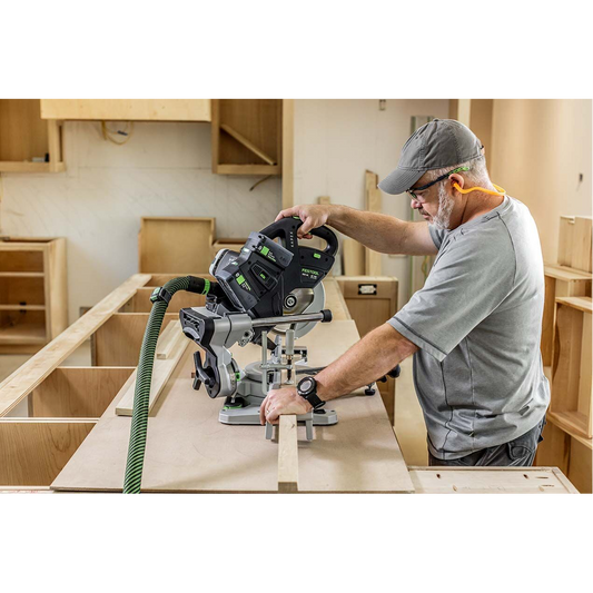 Man using Festool cordless compound miter saw in a woodworking workshop with safety ear protection and dust extraction hose