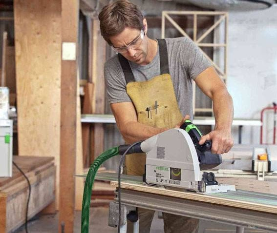 Man wearing safety glasses operating a Festool plungecut saw on wood in a workshop setting