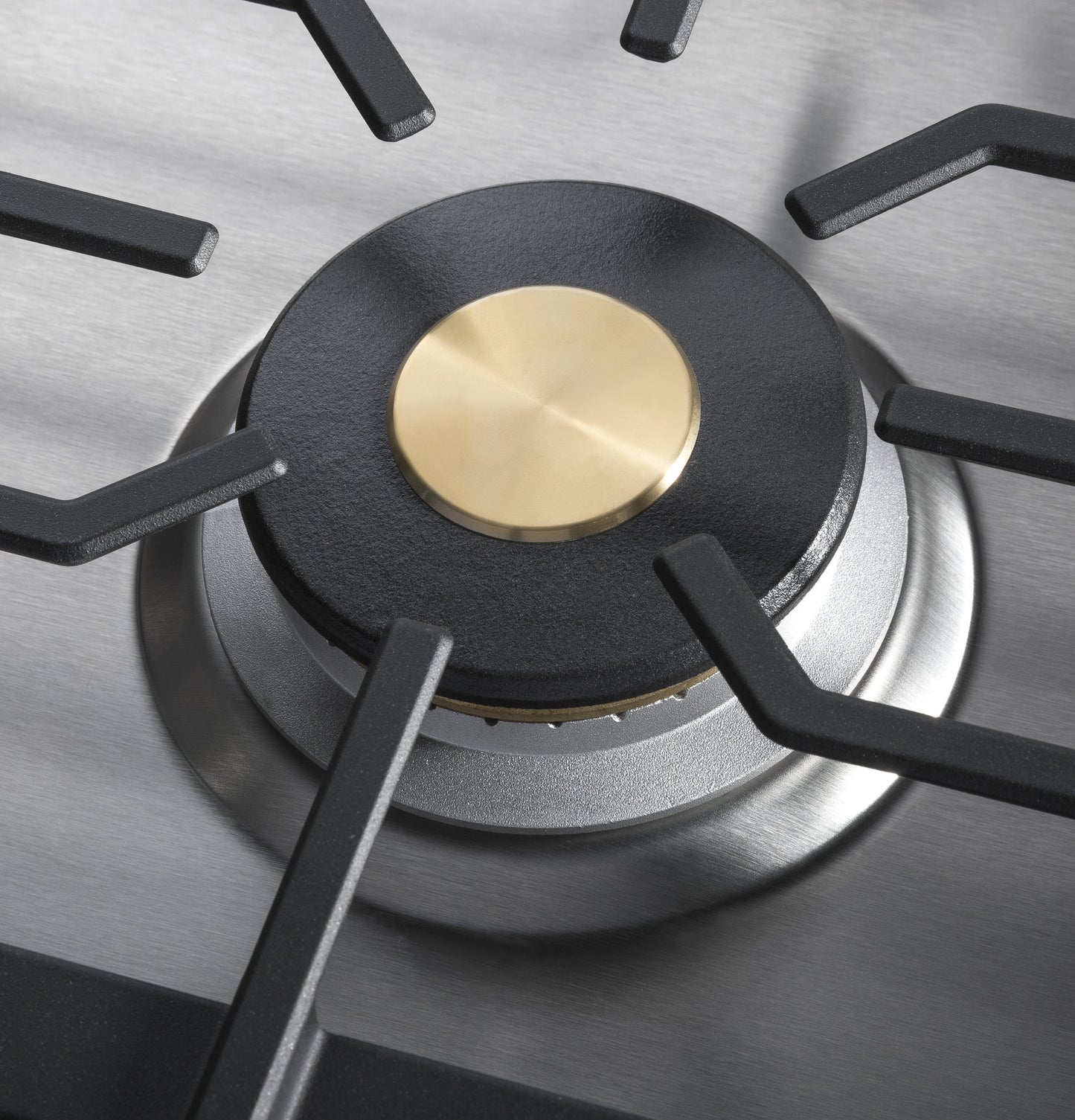 Close-up of brass-capped burner with black cast iron grate on stainless steel cooktop in kitchenware and appliances setting