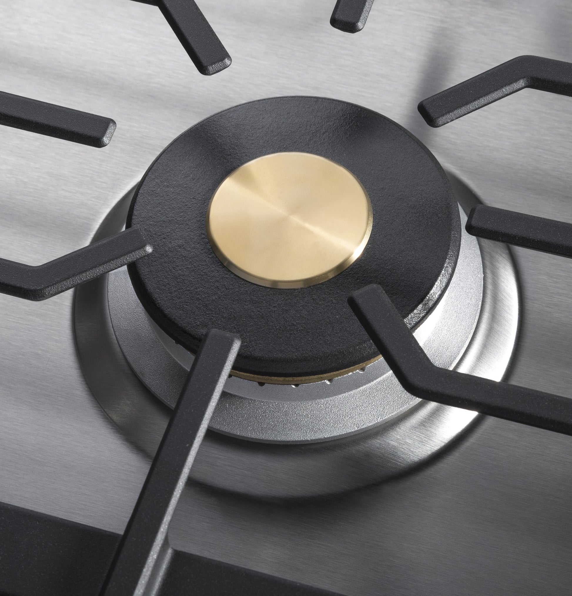 Close-up of brass-capped burner with black cast iron grate on stainless steel cooktop in kitchenware and appliances setting