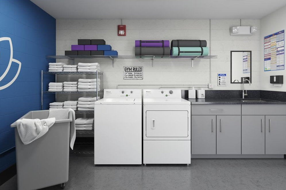 Commercial white top-load washer and dryer in laundry room with folded towels and cleaning supplies in washers collection