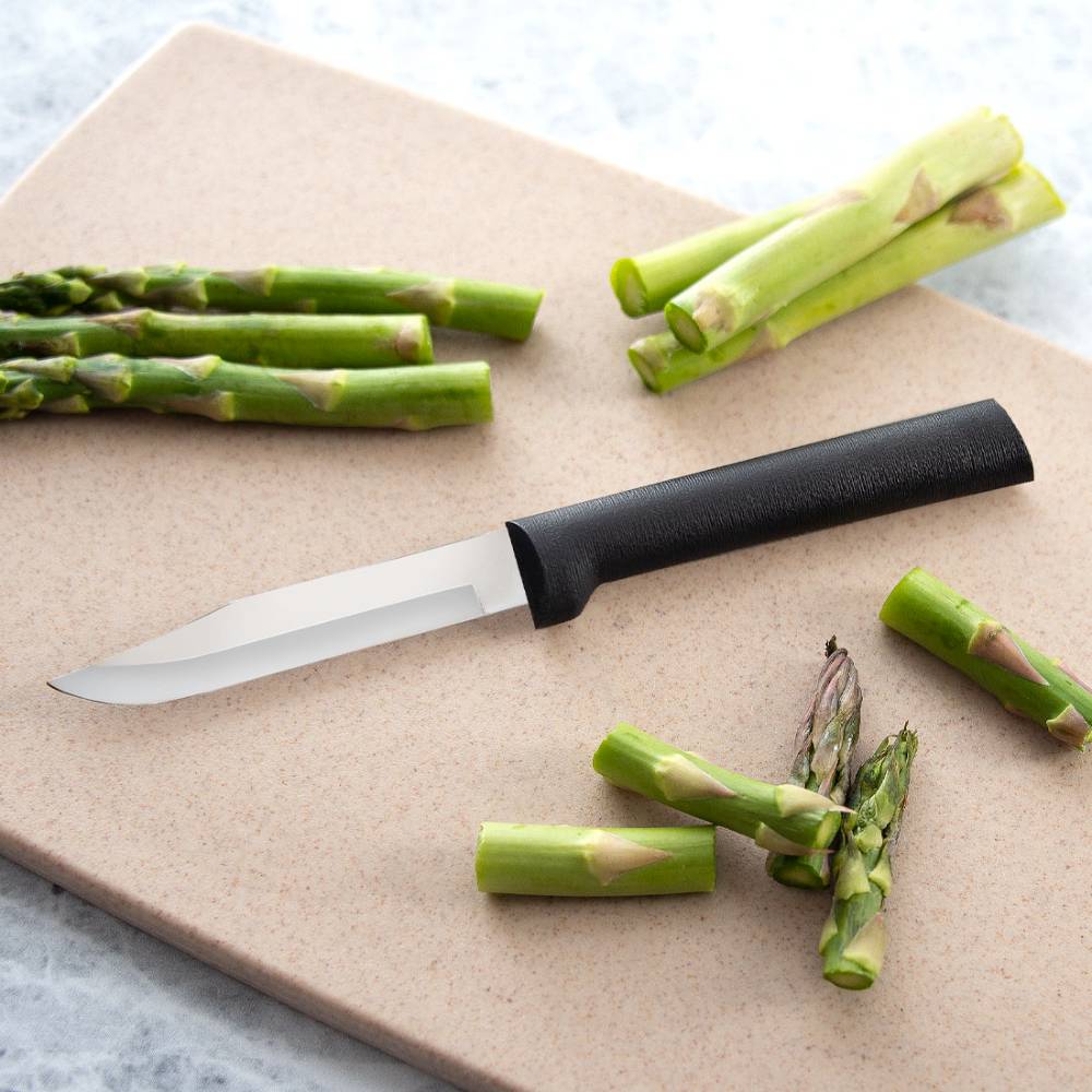 Paring knife with textured black handle and sharp stainless steel blade slicing fresh asparagus on cutting board for kitchen use
