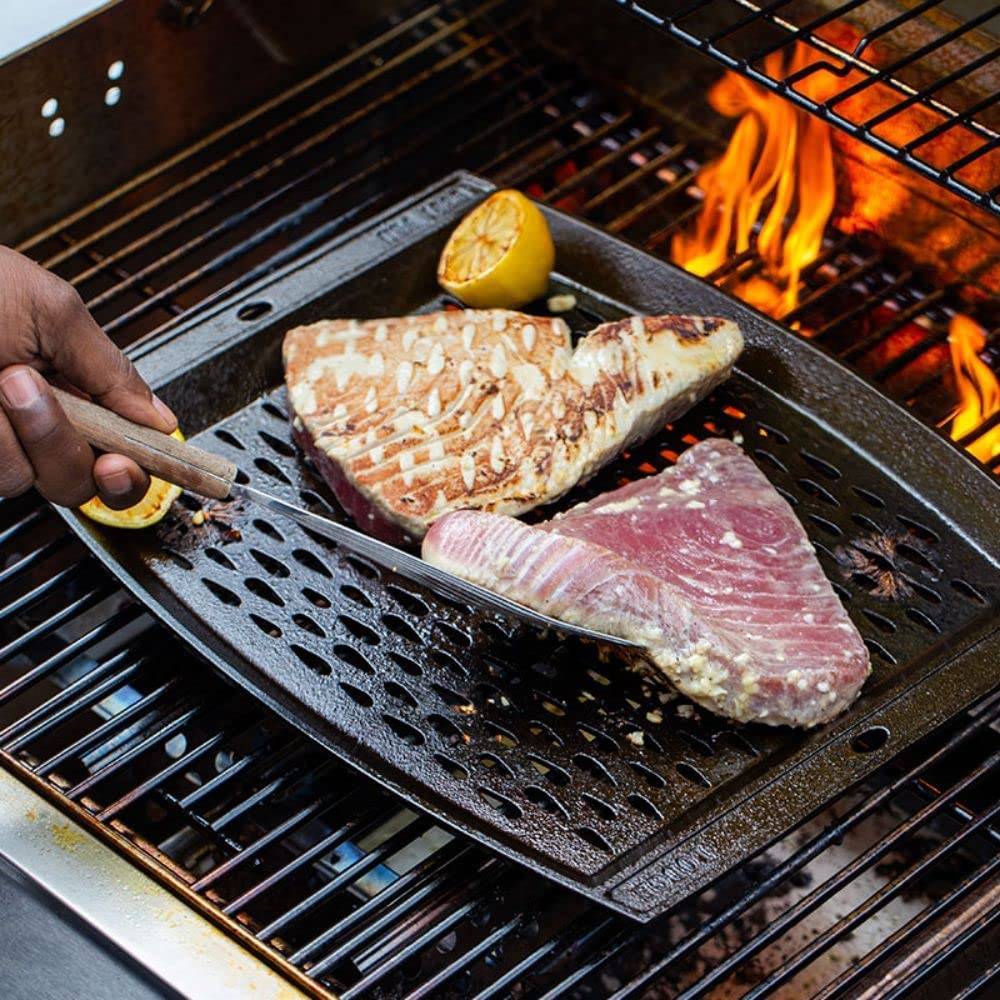 Seasoned cast iron grill topper with perforations cooking two fish fillets and lemon halves over open flame grill
