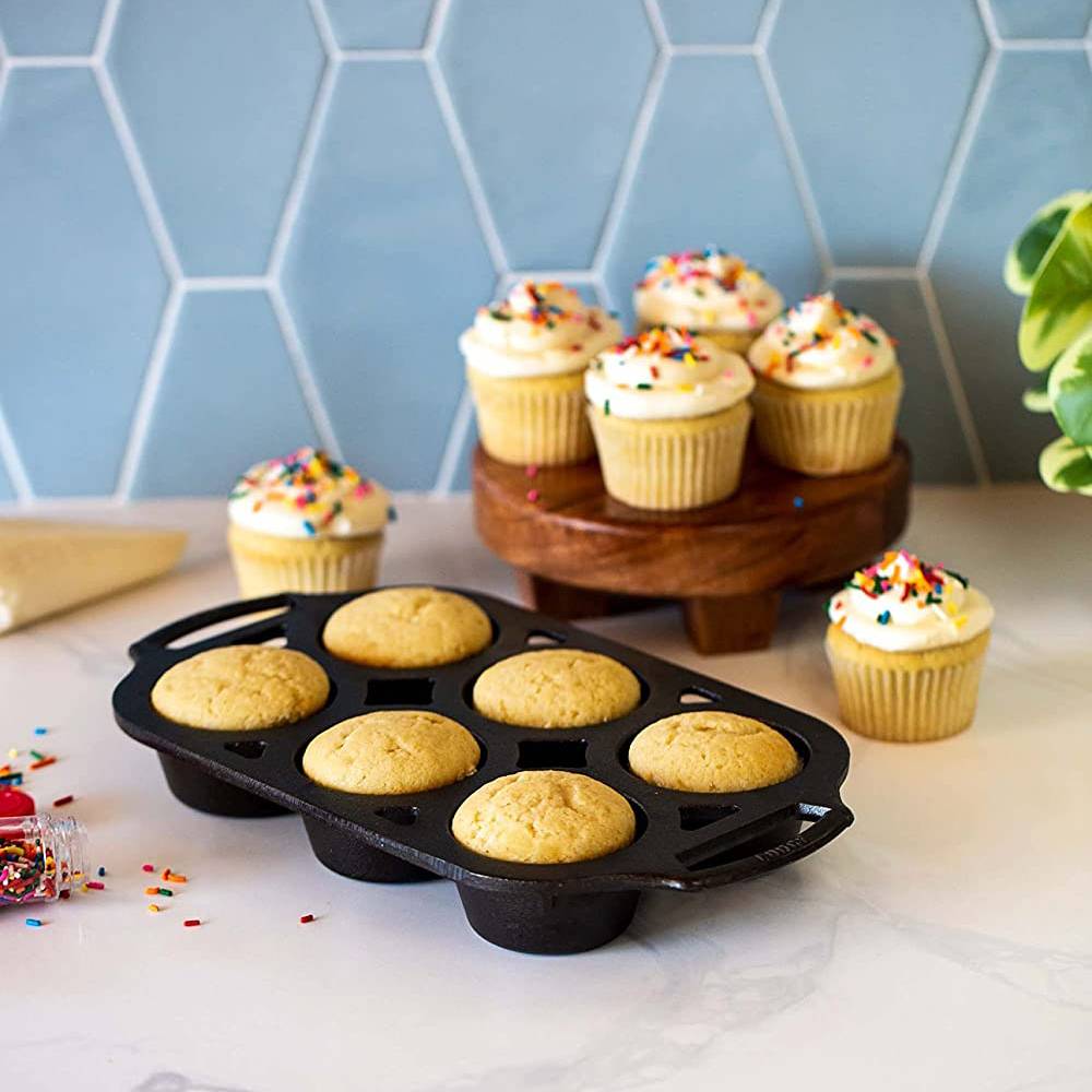 Seasoned cast iron muffin pan with six cups, shown with baked muffins and decorated cupcakes on countertop