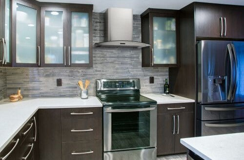 Sleek curved glass chimney hood installed above stainless steel stove with dark wood cabinetry in modern kitchen