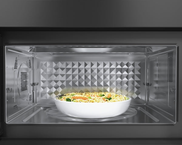 Interior view of black stainless steel microwave cavity with white bowl of food on turntable in kitchen appliances collection