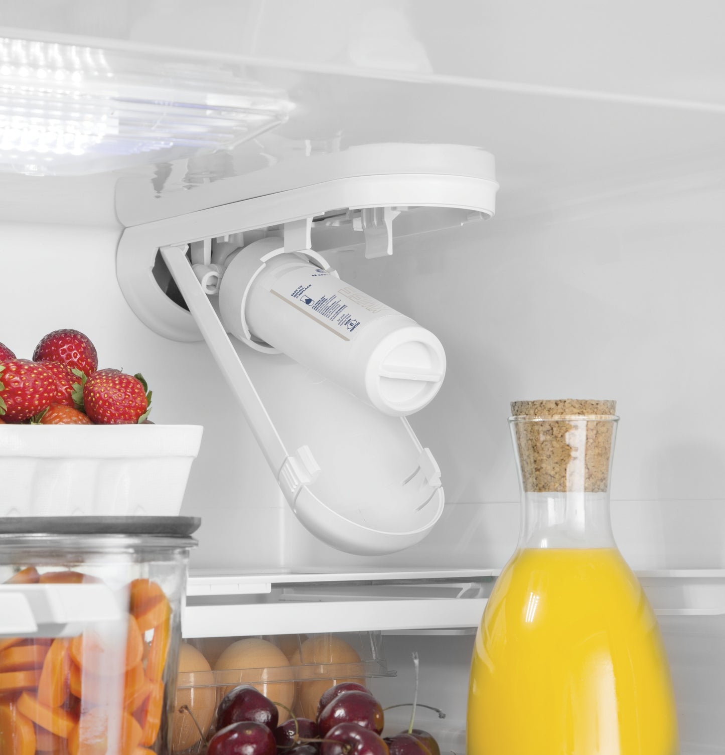 Close-up view of a refrigerator interior showing water filter, fresh fruit, eggs, and a glass jug of orange juice.