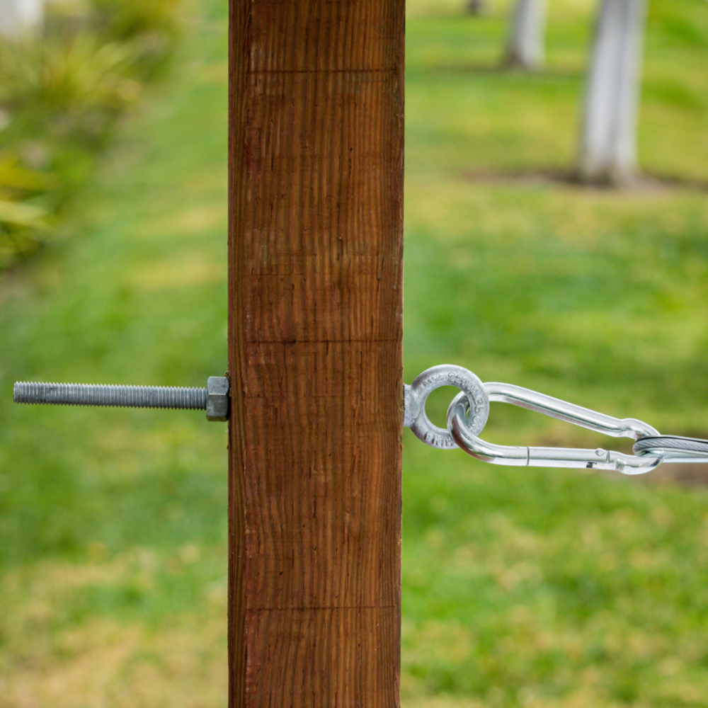 Galvanized eye bolt with shoulder and nut securing wire cable to wooden post for hardware and fasteners use