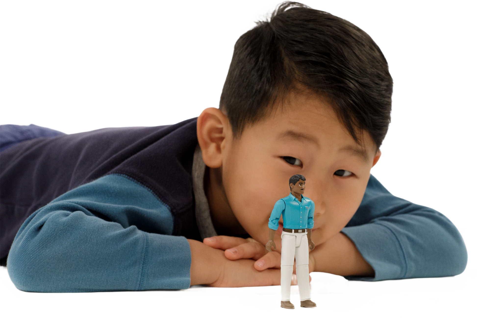 Young boy in blue sweater lying behind articulated male action figure wearing teal shirt and white pants