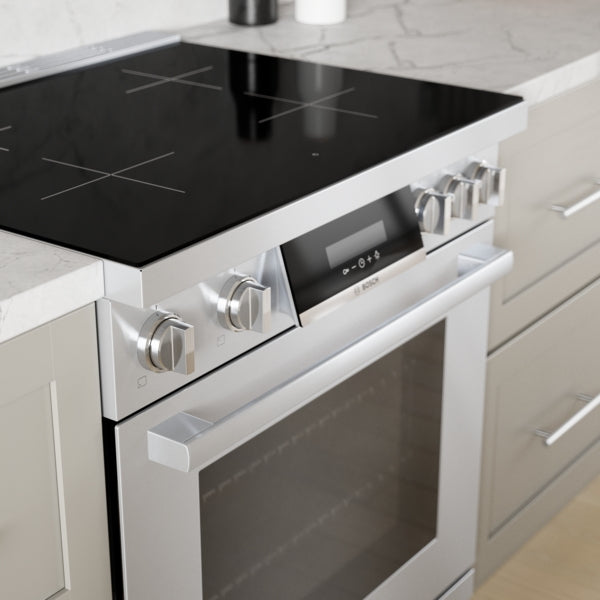 Stainless steel induction freestanding range with smooth glass surface, heavy duty knobs, and ergonomic tilted display in kitchen setting
