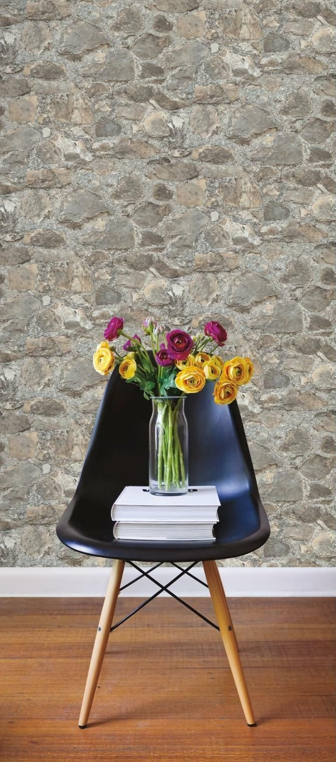 Modern black chair with wooden legs holding a glass vase of flowers and books against a stone textured wall