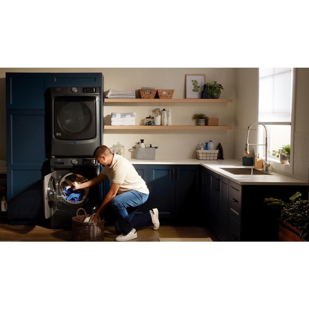 Person loading dark front load washer in modern laundry room with navy blue cabinets and open shelving above