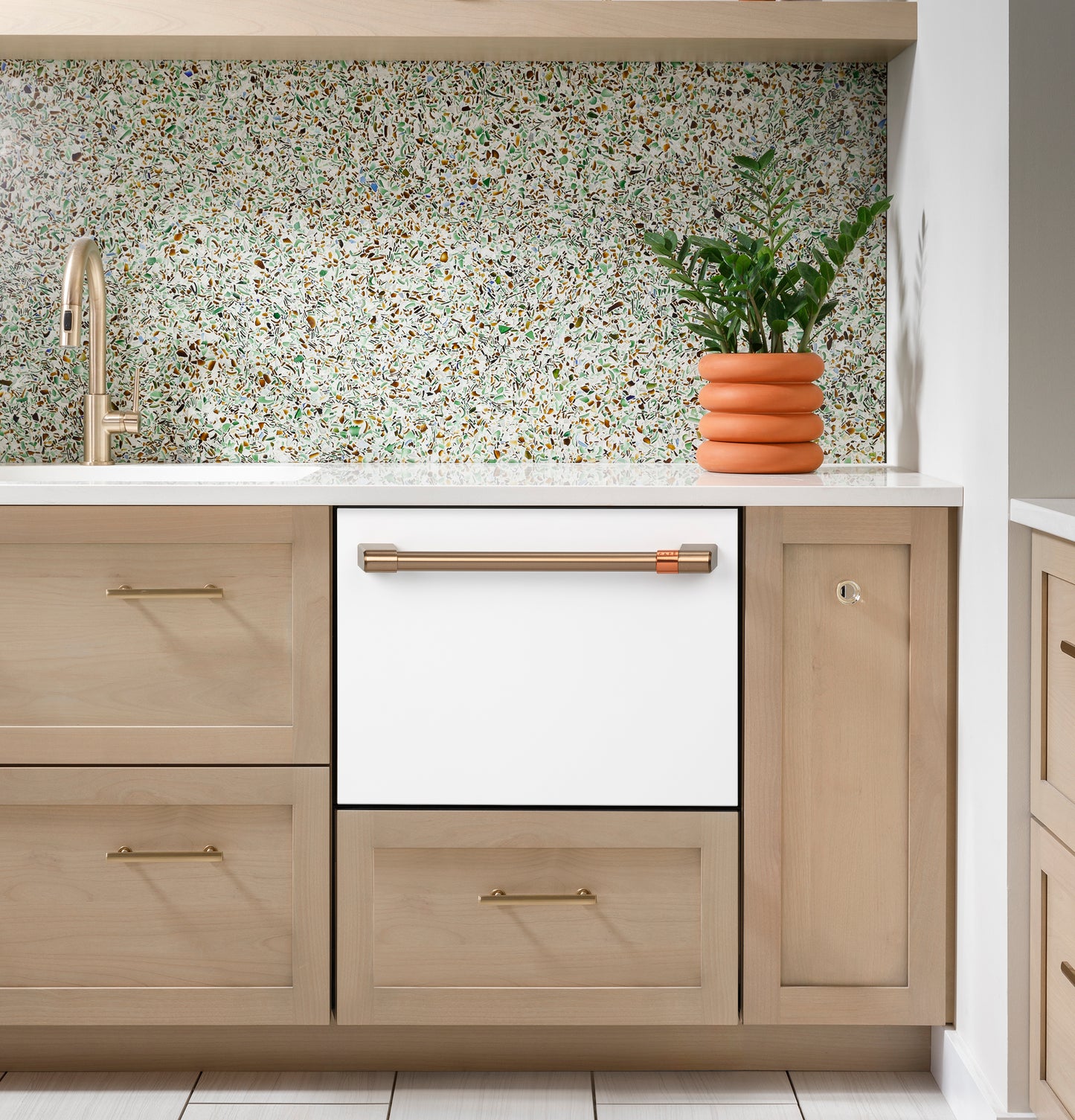 Built-in smart single drawer dishwasher in white with brass handle integrated into modern kitchen cabinetry and terrazzo backsplash