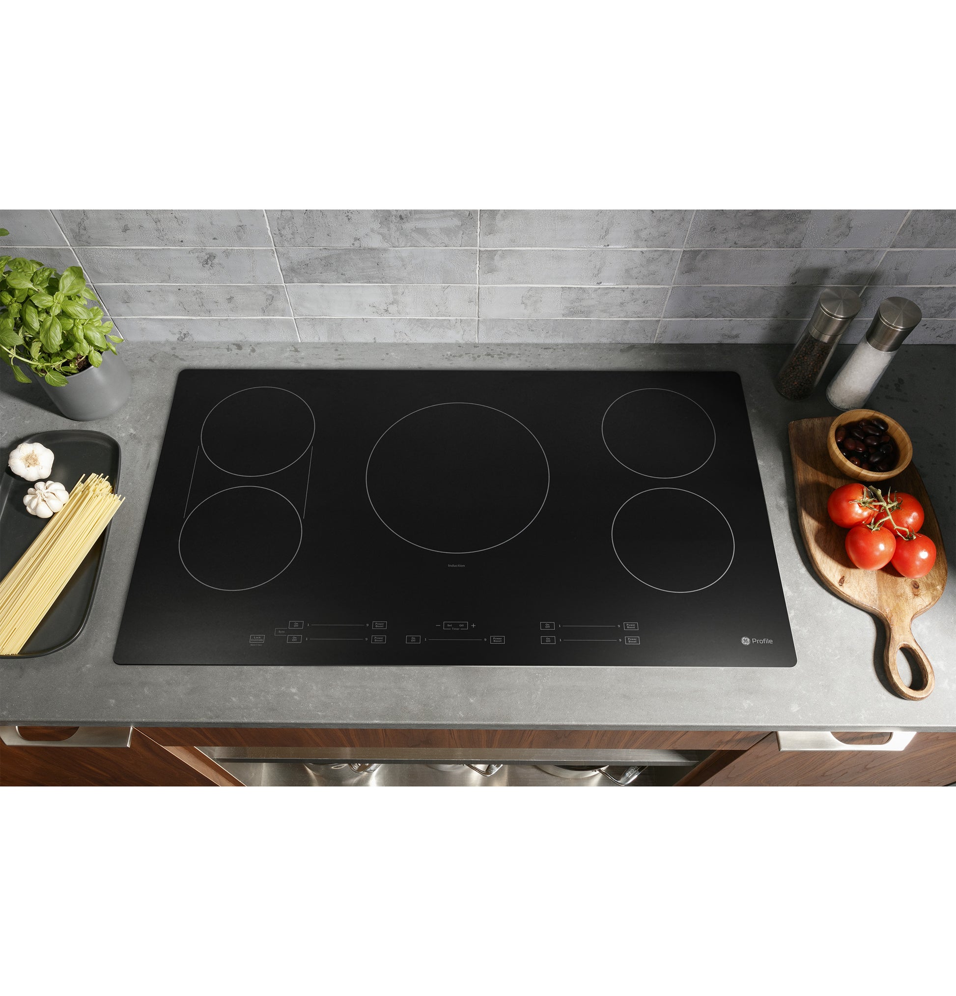 Black built-in induction cooktop with five cooking zones set in modern kitchen countertop with fresh ingredients nearby