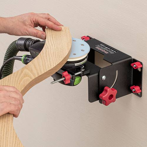 Black metal tilting sander base with red knobs mounted on wall, sanding curved wood piece for home improvement use