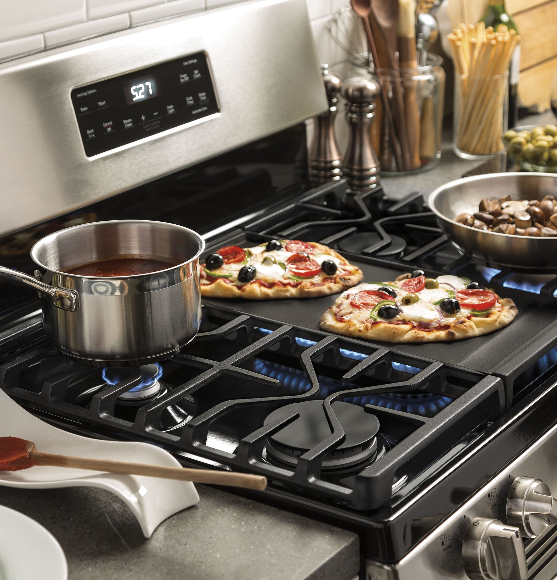 Stainless steel pot simmering sauce and two small vegetables pizzas cooking on burners of freestanding gas range
