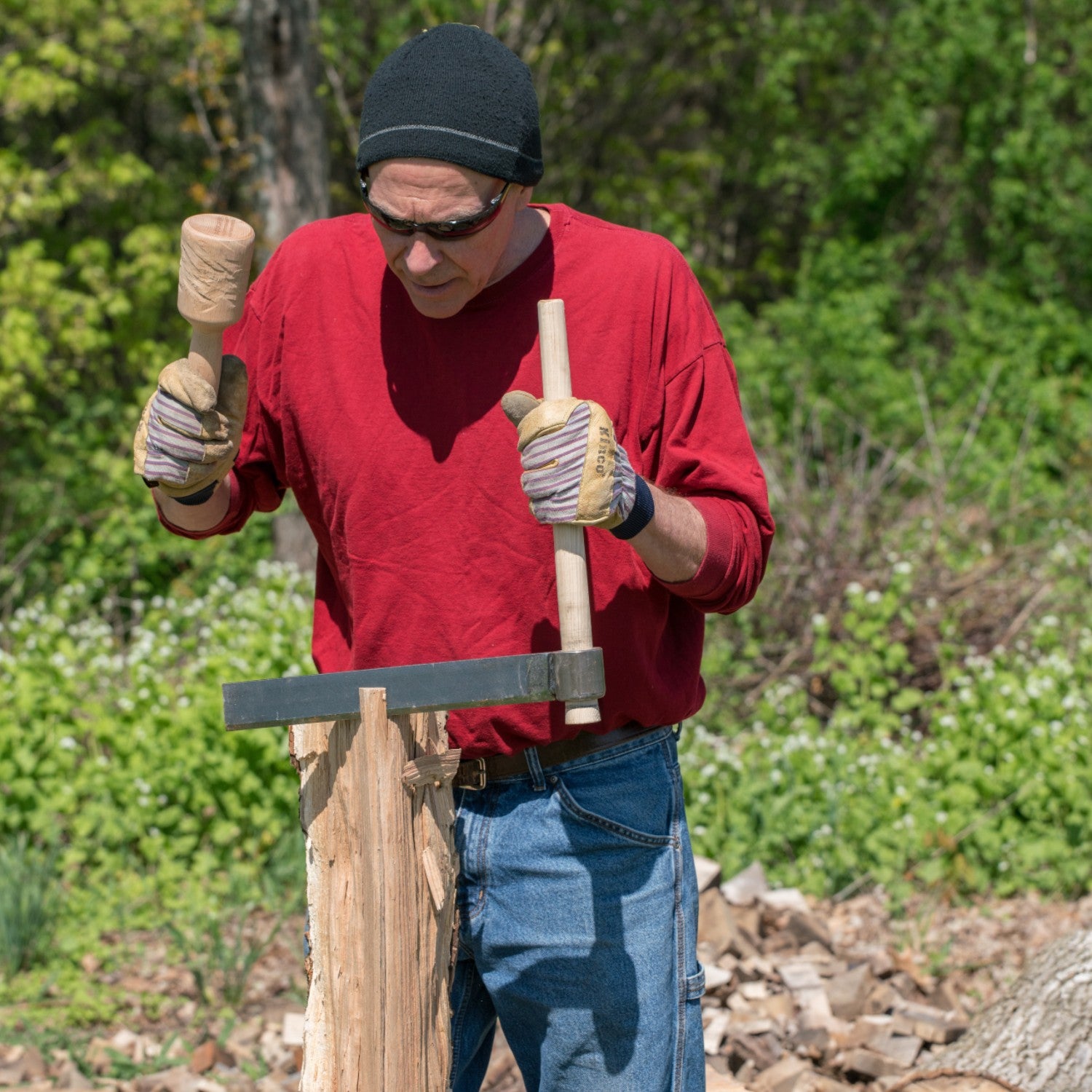 Man wearing gloves using wood splitting froe and mallet on log outdoors in tool accessories and home improvement collection