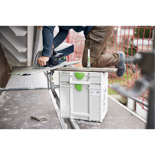 Person using a Festool power saw mounted on a guide rail supported by a white and green modular storage system on a construction site floor, demonstrating tool storage and woodworking efficiency.