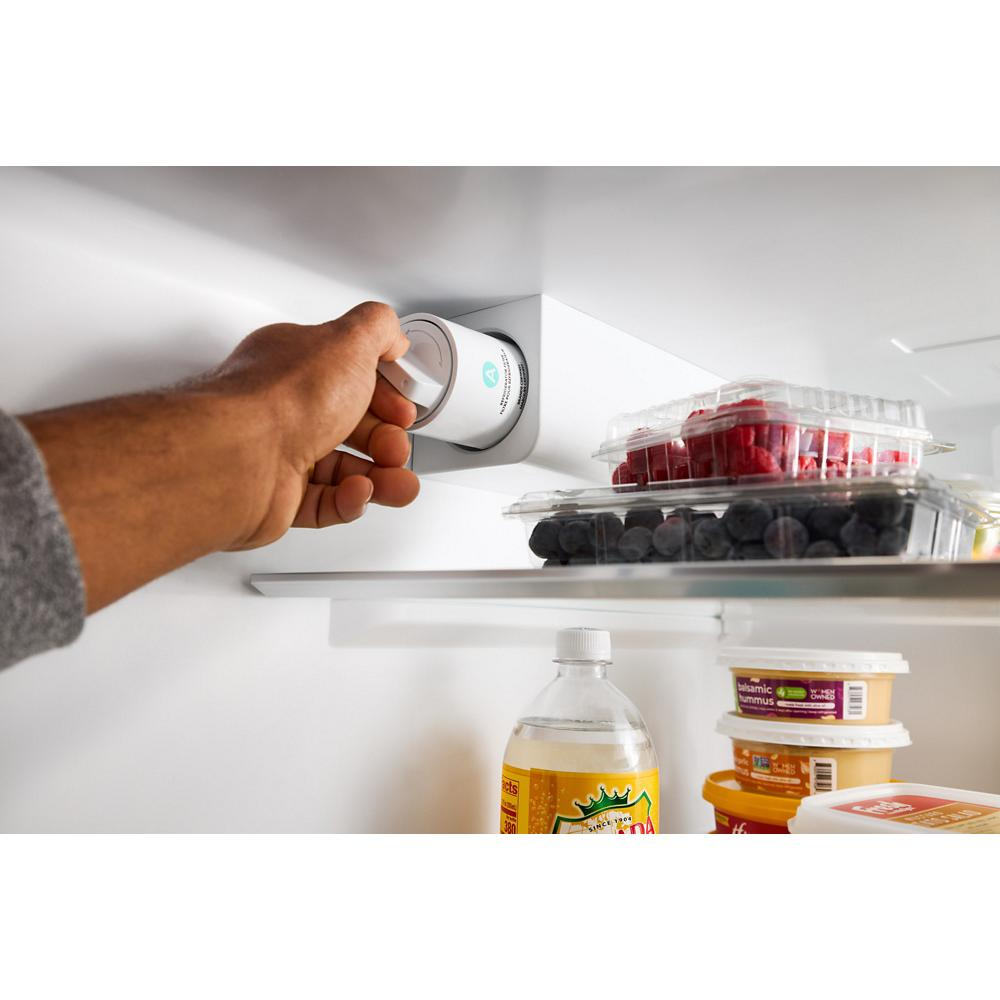 Hand adjusting temperature control knob inside white Whirlpool French door refrigerator with food containers and beverages