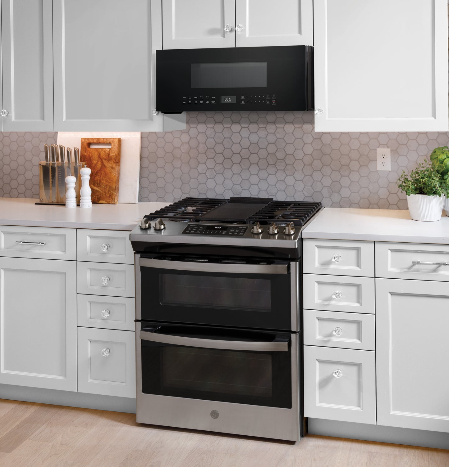 Black low-profile sensor microwave installed over stainless steel double oven range in modern kitchen appliances setting