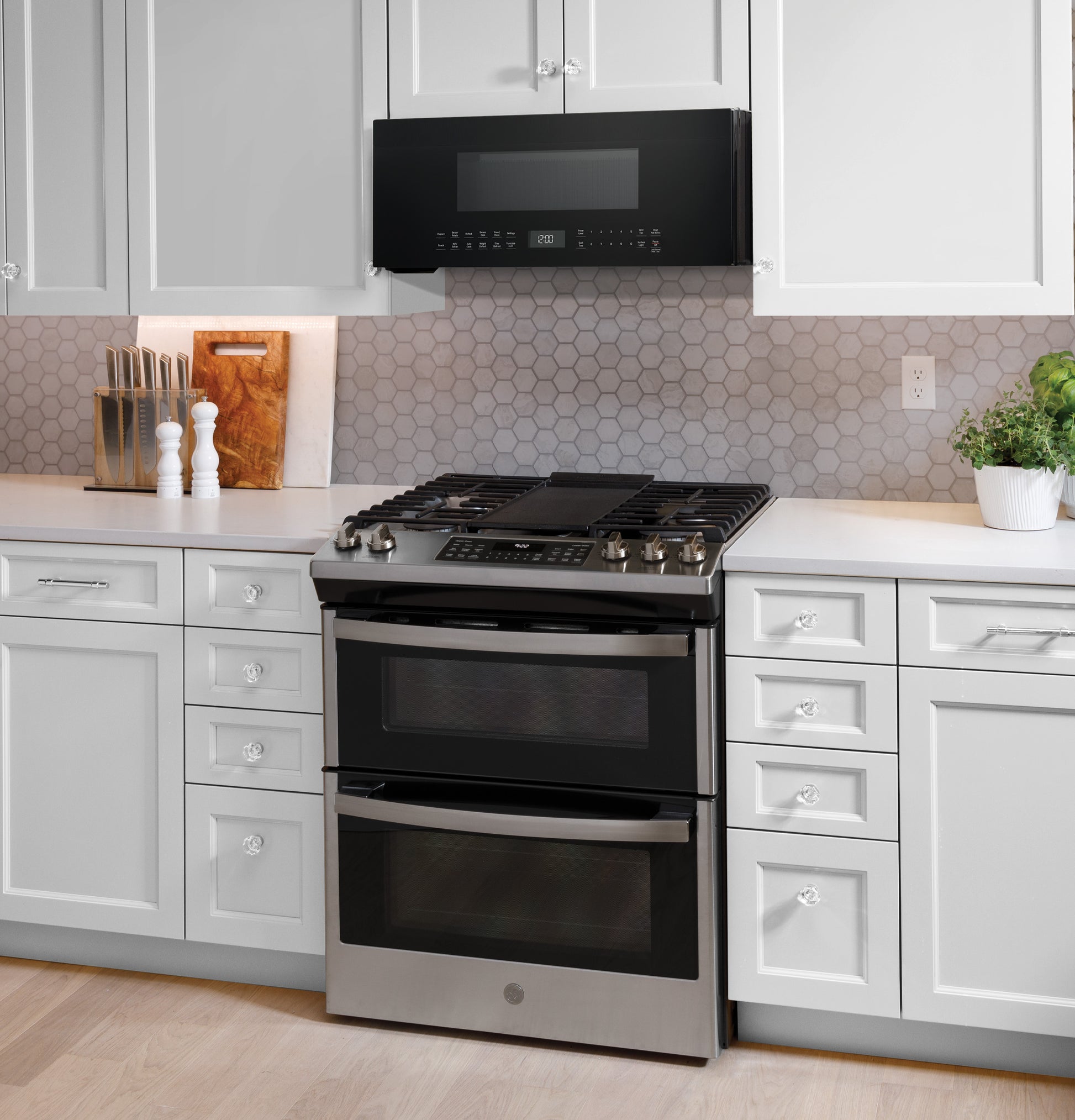 Black low-profile sensor microwave installed over stainless steel double oven range in modern kitchen appliances setting