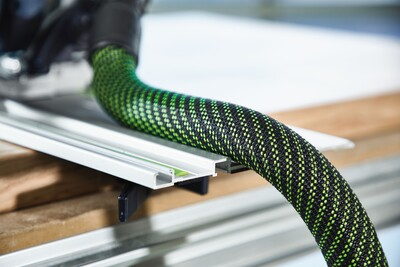 Green and black anti-static vacuum hose attached to woodworking dust extractor in workshop setting
